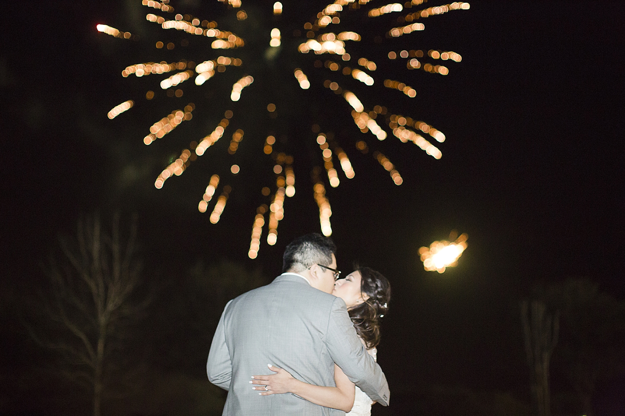 bride and groom kiss in front of fireworks